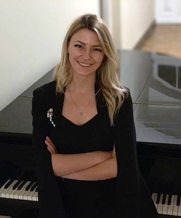Oksana Karataj, šypsodamasi, stovi prie juodo koncertinio fortepijono